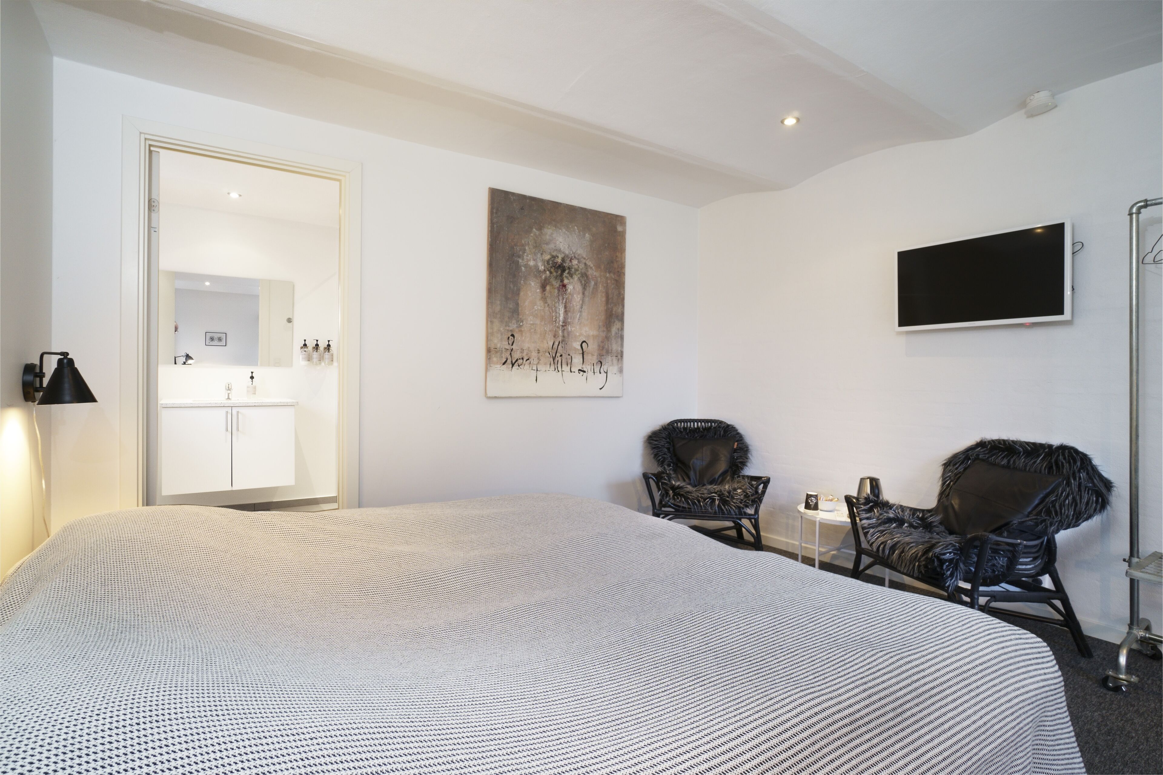A hotel room with a large bed, two armchairs, a flat-screen TV, a painting, and a mirror.