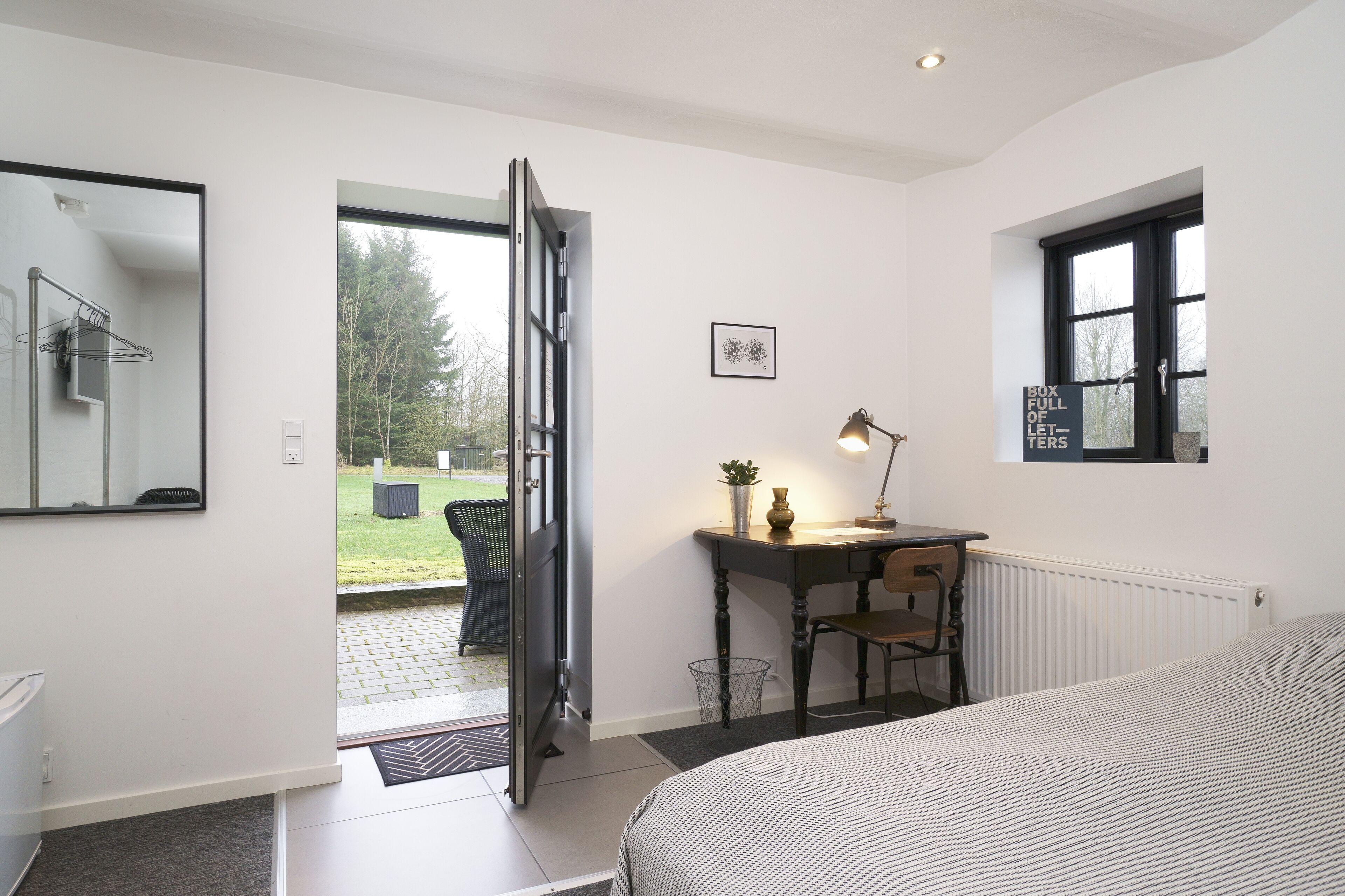 Un dormitorio con cama, escritorio, silla, ventana y puerta que da a un balcón.