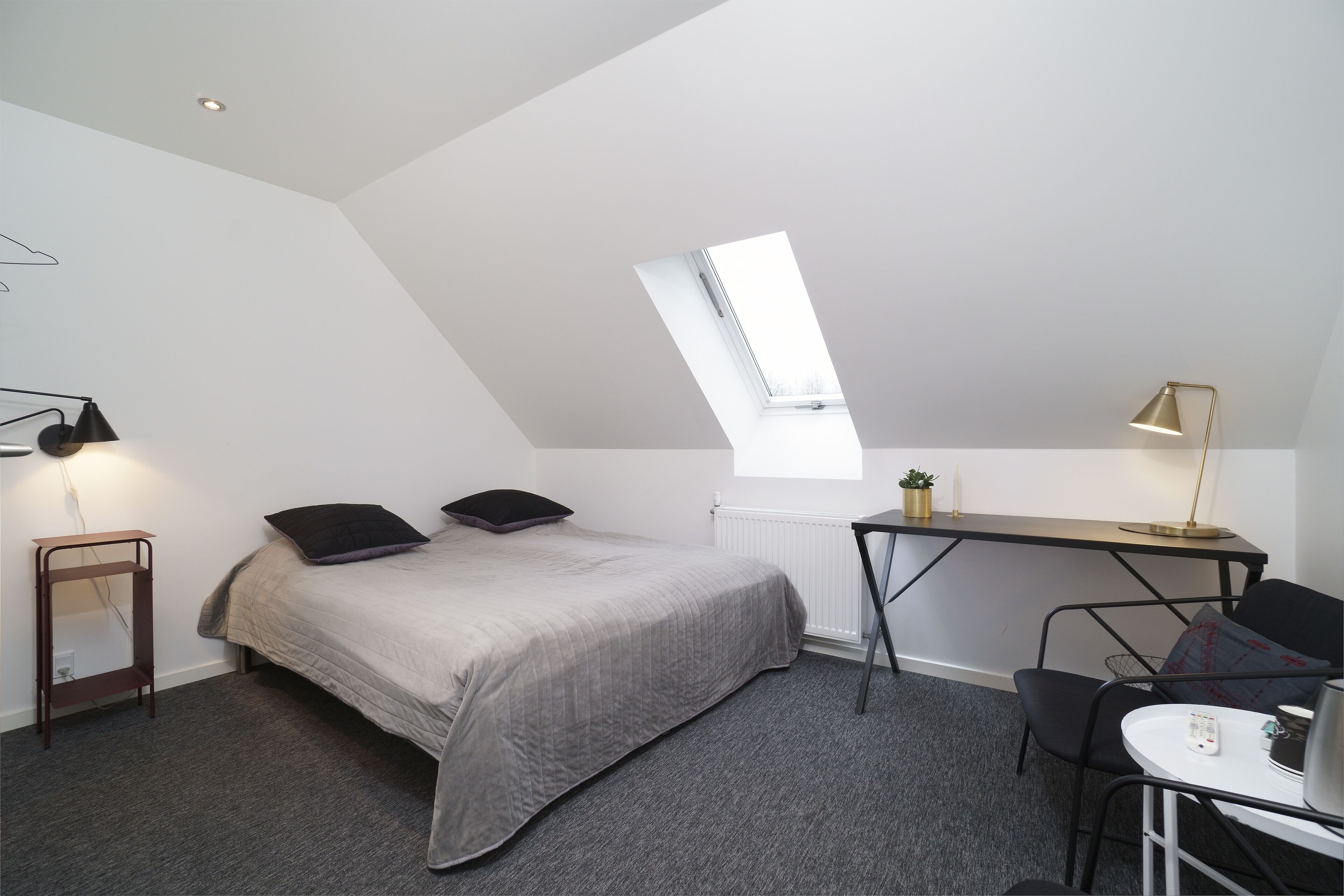 Ein kleines Zimmer mit Bett, Schreibtisch, Stuhl und einem Oberlicht.