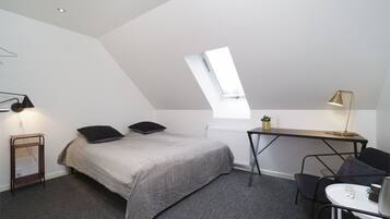 Een kleine kamer met een bed, een bureau, een stoel en een dakvenster.
