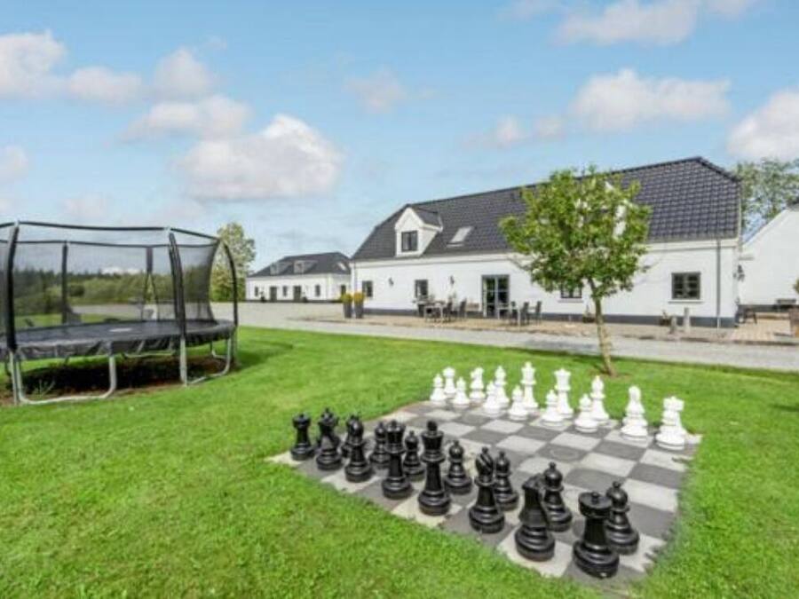A chessboard set up on a grassy lawn with a swing set nearby, in front of a white building with a sloped roof.