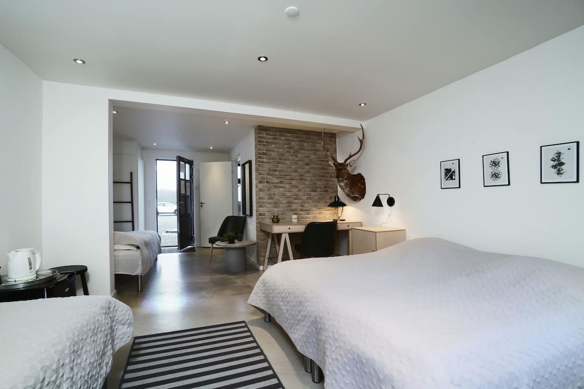 A modern hotel room with a large bed, a desk, a chair, and a brick accent wall.