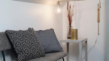 Una sala de estar moderna con un sofá gris, cojines estampados, una mesita auxiliar blanca y una lámpara de pie.