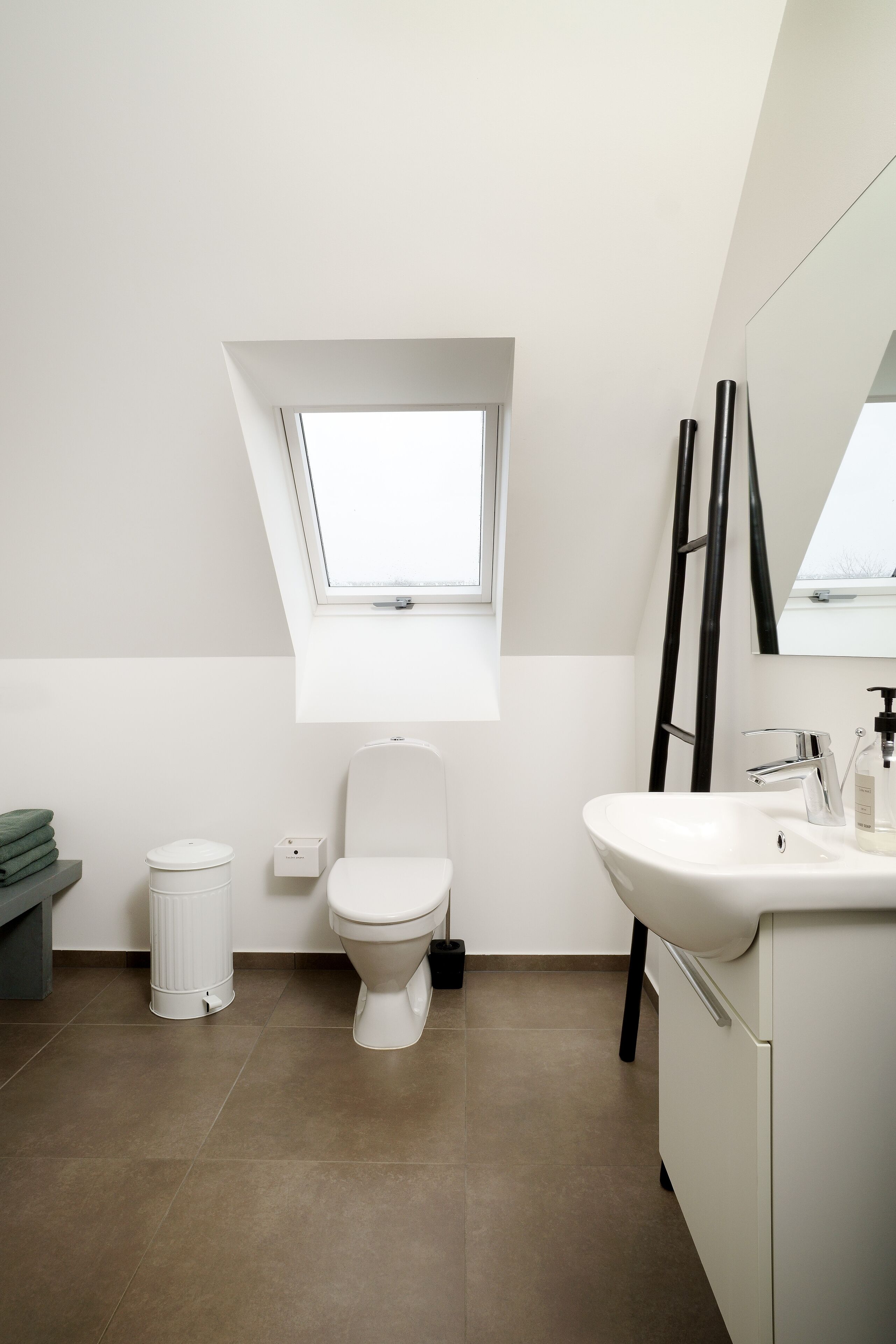 Un baño moderno con tragaluz, inodoro, lavabo y un cesto de basura.