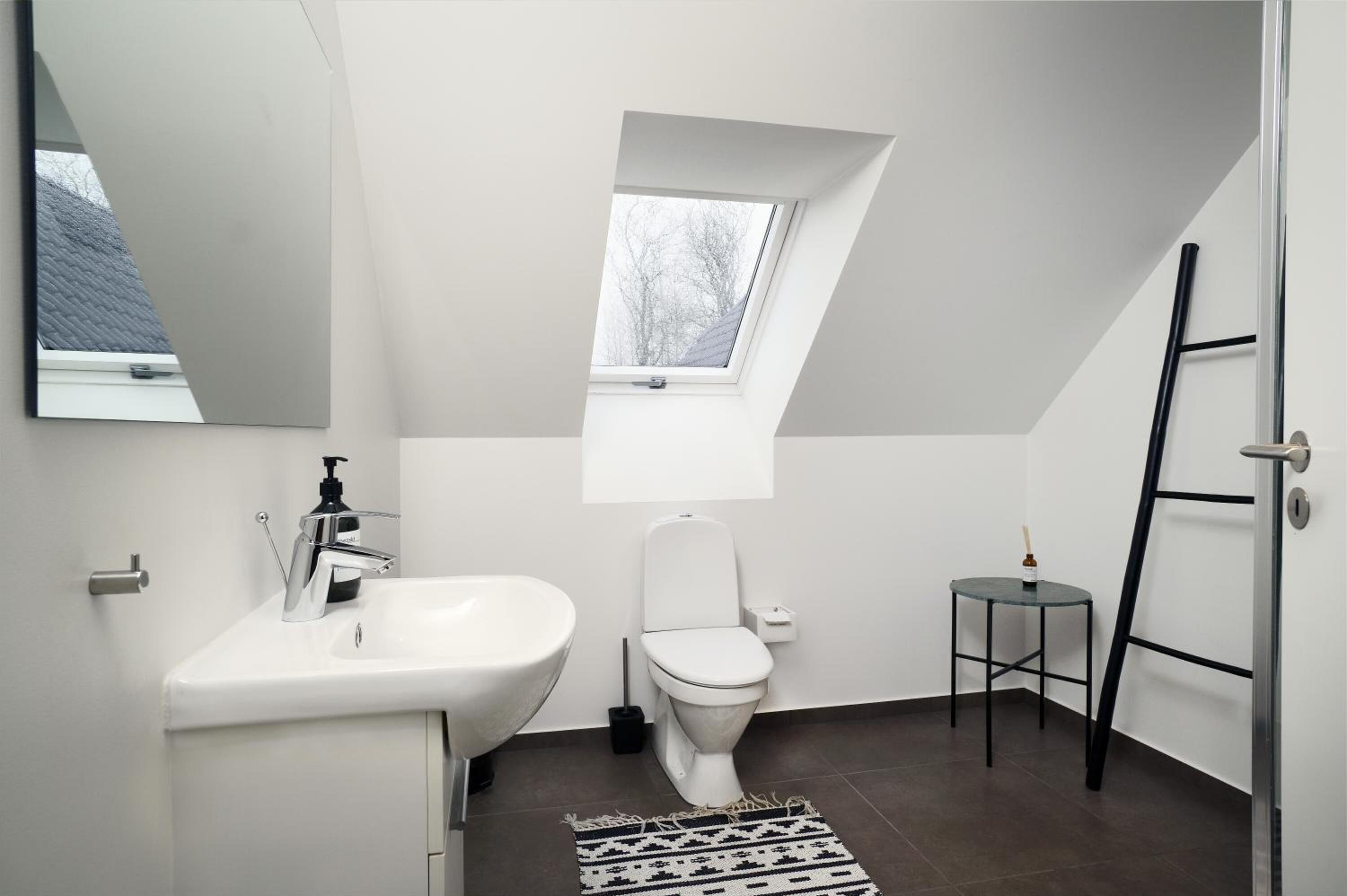 A modern, compact bathroom with a white sink, toilet, and a small window.