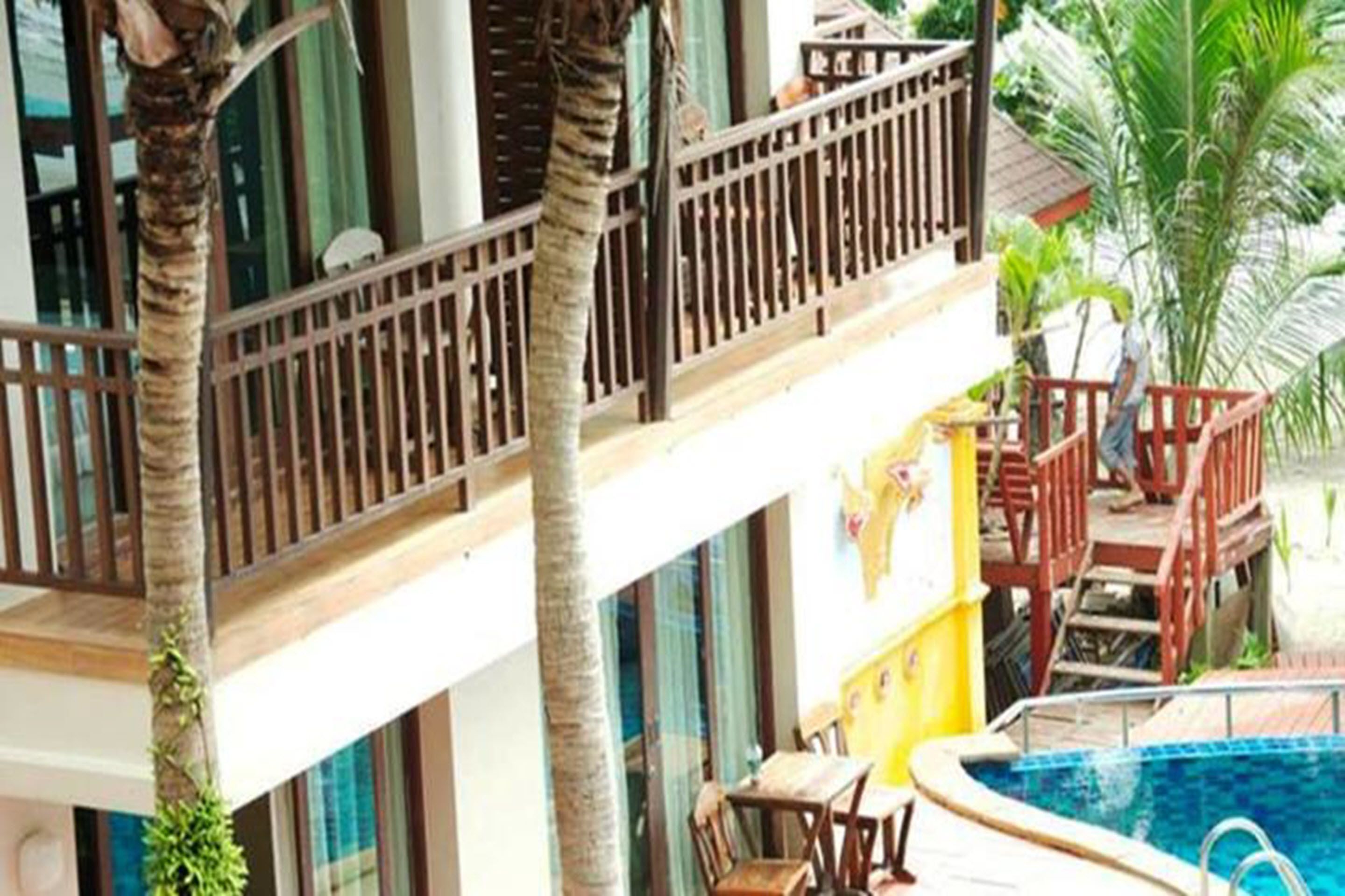 Un edificio de varios pisos con piscina, mobiliario exterior y palmeras.