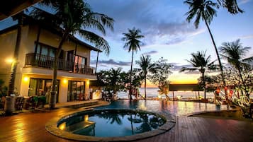 Un resort con piscina, palmeras y vista al océano al atardecer.
