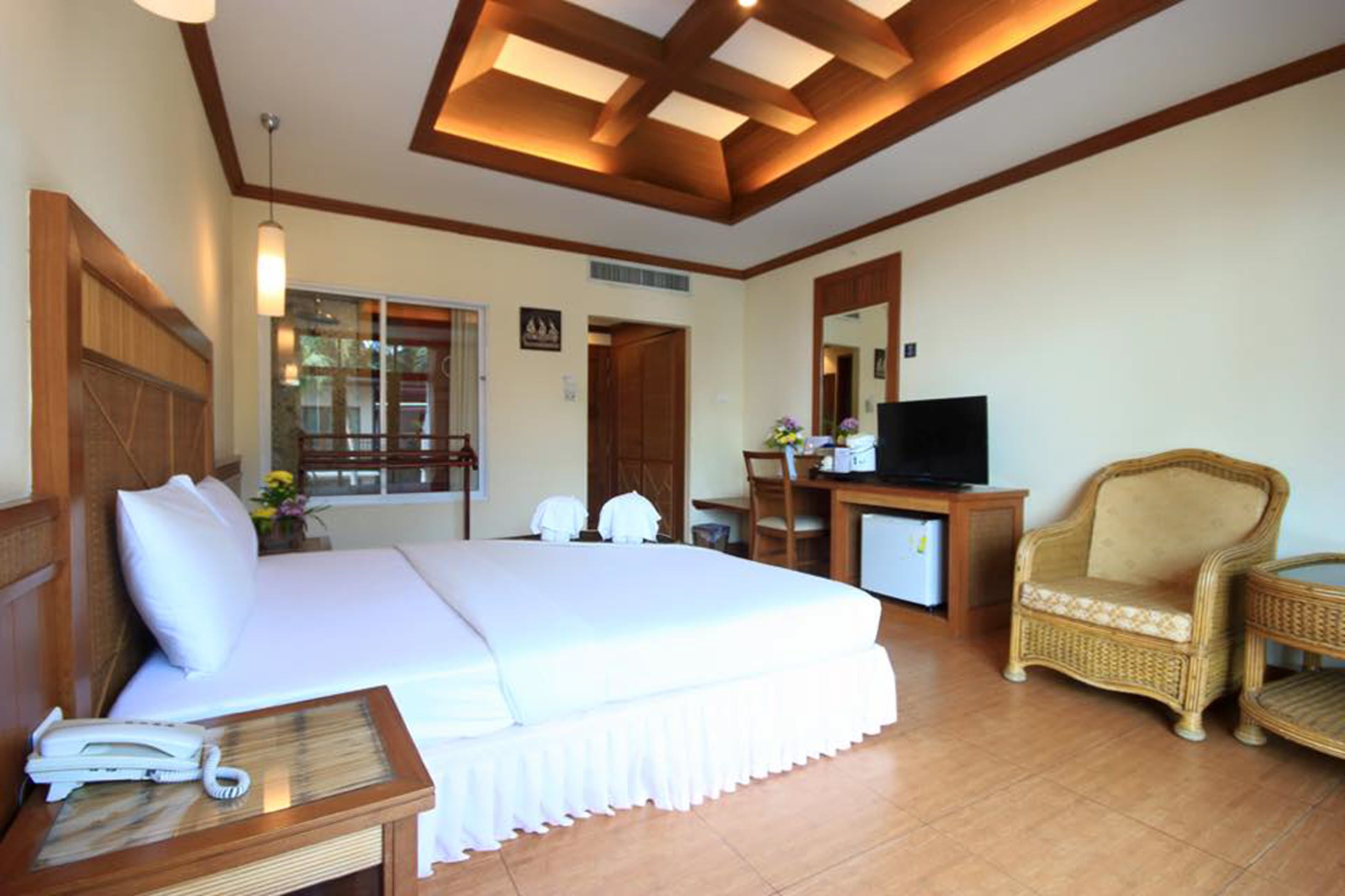 Una habitación de hotel con una cama grande, un escritorio con ordenador, televisor y muebles de mimbre.