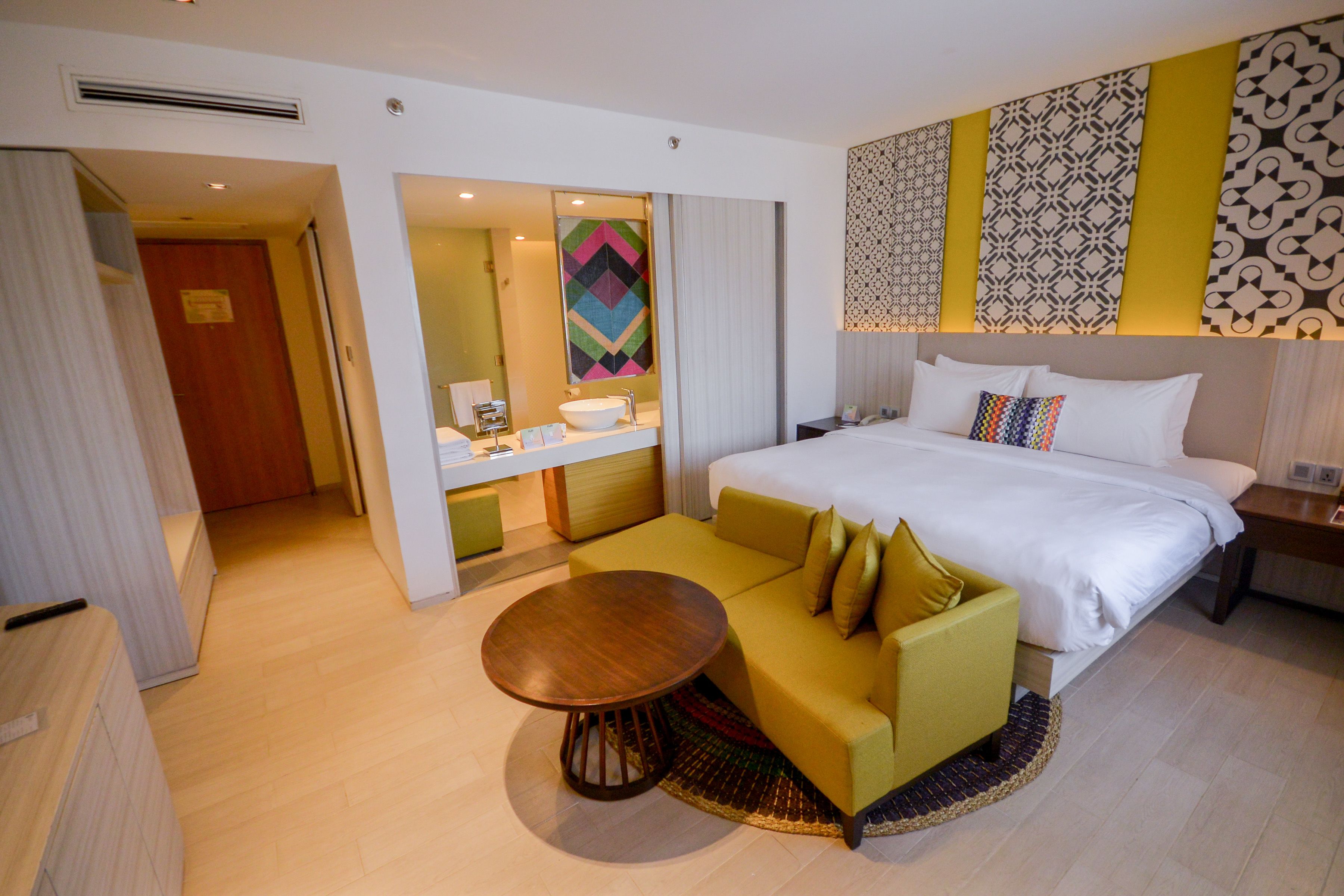 Ein Hotelzimmer mit Bett, einer Couch, einem runden Tisch, einem Badezimmer mit Waschbecken und einem Spiegel.