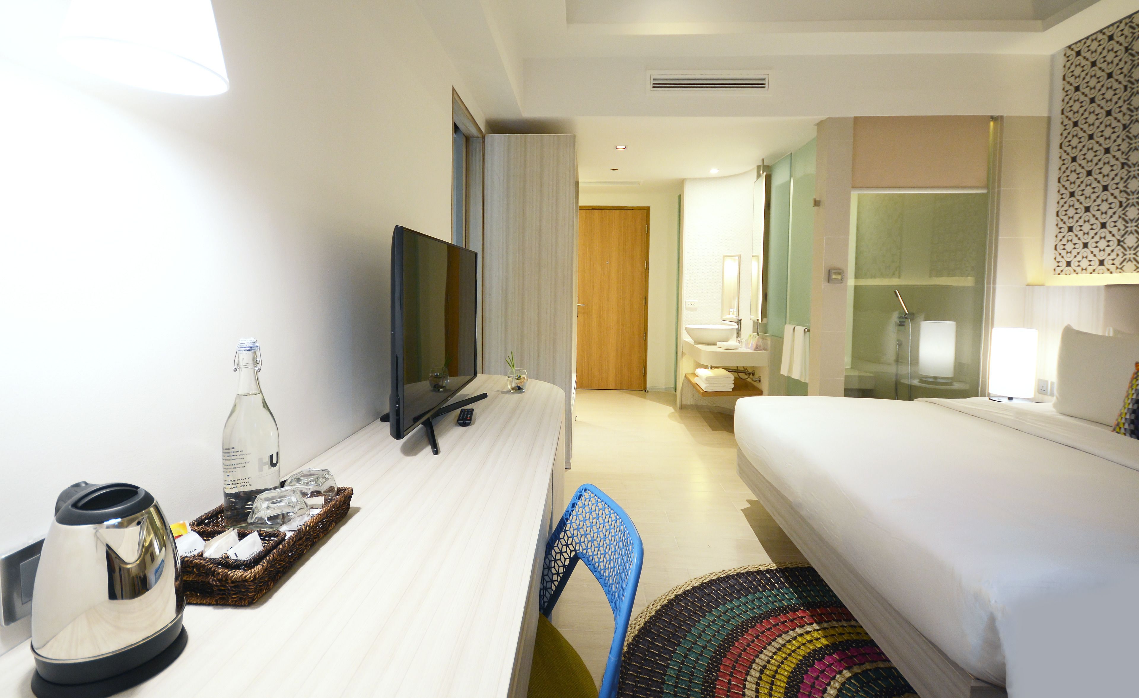 A hotel room with a bed, a desk with a television, a bottle, and a kettle.