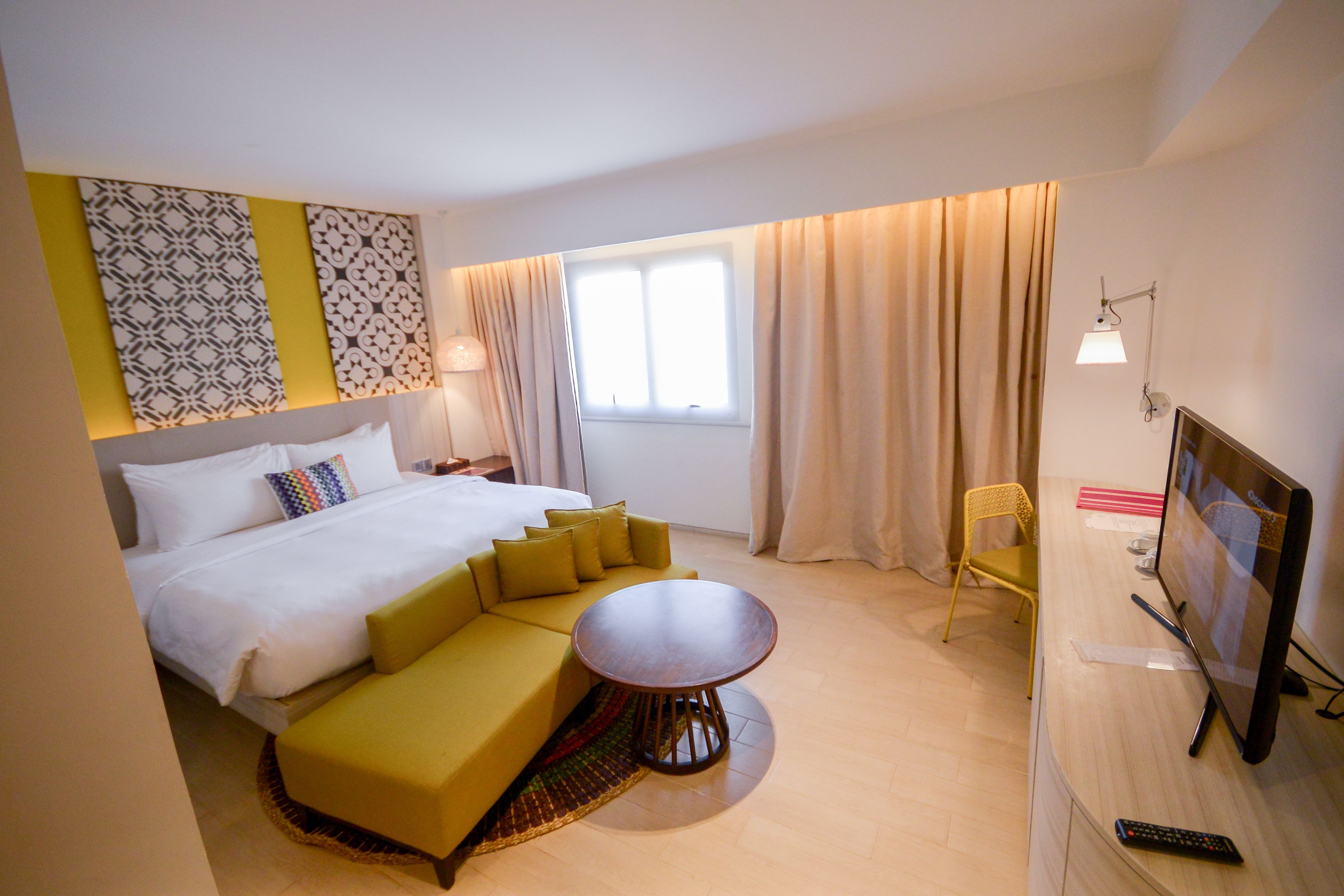 A hotel room with a bed, a sofa, a small table, a chair, a TV, and a window with curtains.