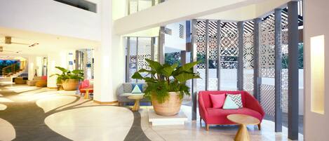 A spacious lobby with a modern design, featuring a red sofa, a large potted plant, and a wooden coffee table.
