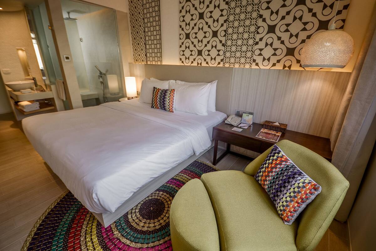 A hotel room with a large bed, a bedside table with a lamp, a chair, and a patterned rug.