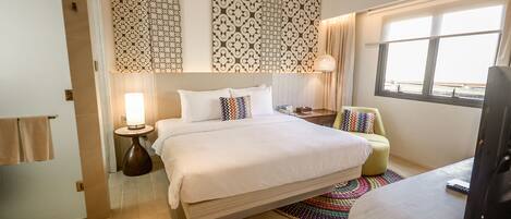 A hotel room with a large bed, a desk, a chair, a lamp, and a window.