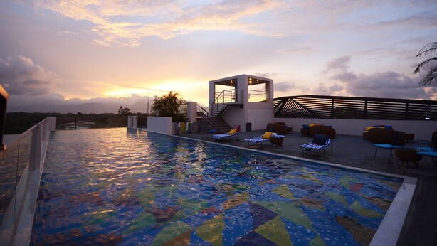 A rooftop pool with a view of the sunset, lounge chairs, and a small structure with stairs. - Hue Hotels and Resorts Puerto Princesa Managed by HII (Puerto Princesa)