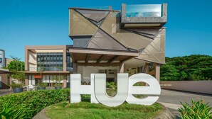 A modern building with a large 'HUE' sign in the foreground, surrounded by greenery and a clear sky. - Hue Hotels and Resorts Puerto Princesa Managed by HII (Puerto Princesa)