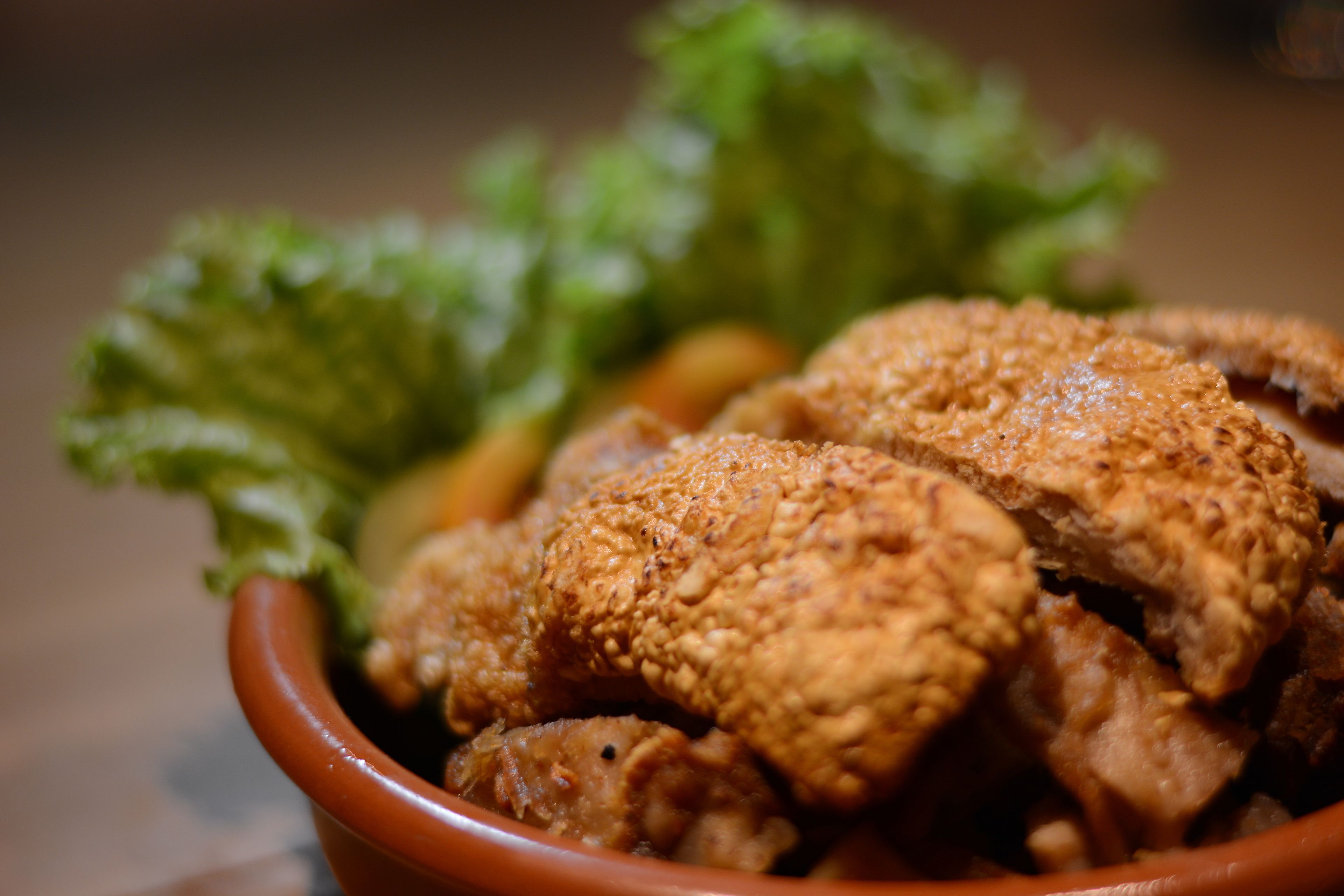 A bowl of fried chicken with crispy coating and a side of green leafy vegetables.