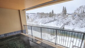 Ett bubbelbad med ett stengolv, ett träpanelat tak och utsikt över ett snötäckt landskap genom en balkongräcke.