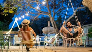 Un'area patio con sedie in vimini, una sedia a dondolo, luci a stringa e un grande albero.