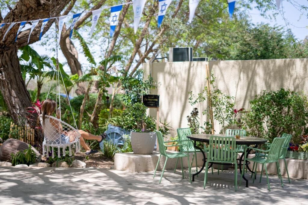 An outdoor patio with a swing, green chairs, and a table.