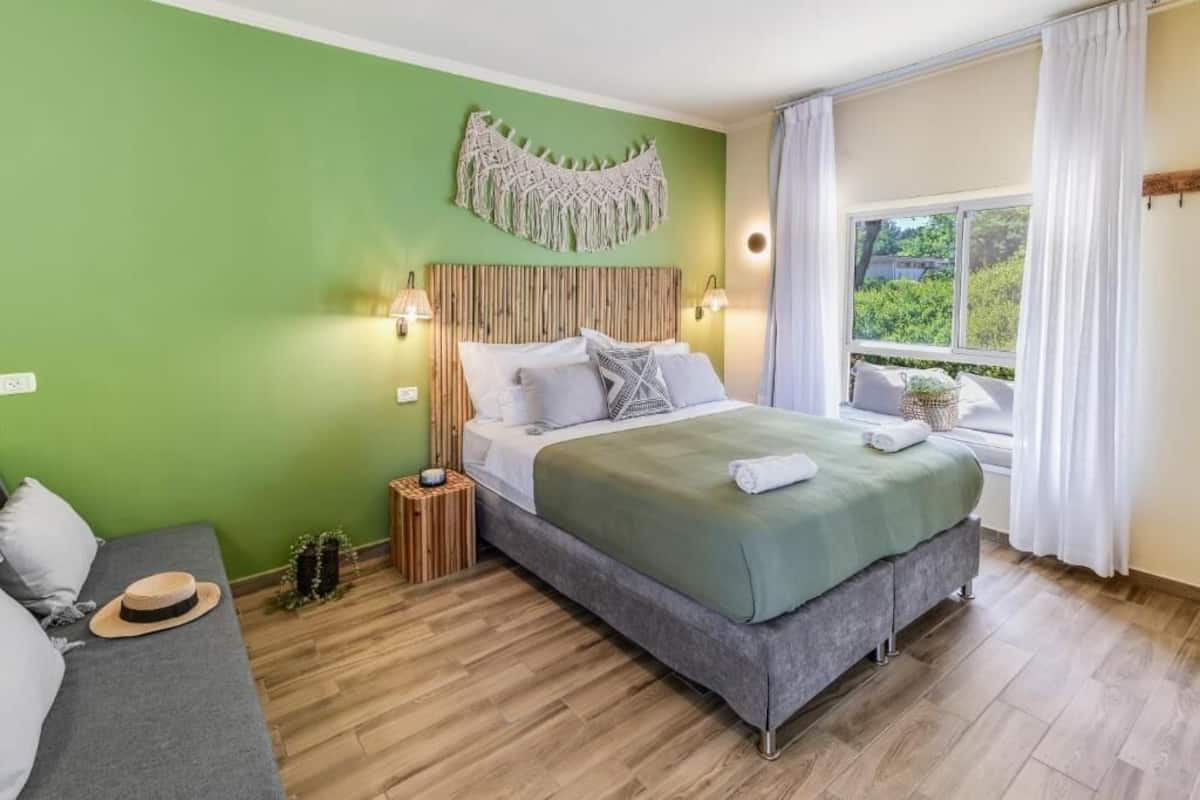 A bedroom with a bed, bedside lamps, a green wall, a window with curtains, and a small plant.