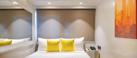 A modern hotel room with a large bed, two yellow pillows, a bedside table with a phone, and a cityscape painting on the wall.