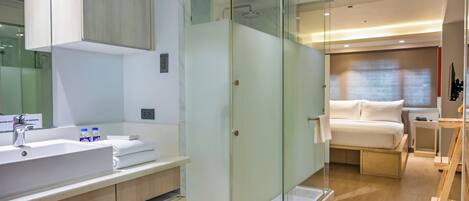 Une salle de bain moderne avec une douche à parois de verre, un lavabo avec un miroir et une table de chevet avec une lampe.