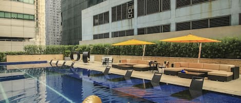 A swimming pool with a golden inflatable swan, surrounded by modern buildings and outdoor seating areas.