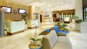 A modern hotel lobby with a reception desk, seating area, and a staircase leading to upper floors. - Grand Livio Kuta Hotel (Legian)