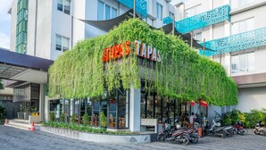 A hotel with a green logo, a restaurant named "Tapas" with outdoor seating, and several motorcycles parked in front. - Grand Livio Kuta Hotel (Legian)