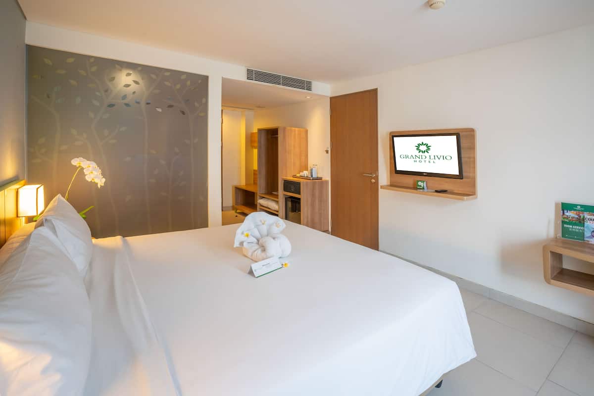 Hotellihuone, jossa on sänky, yöpöytä lampun kanssa, seinälle asennettu televisio ja puinen vaatekaappi.