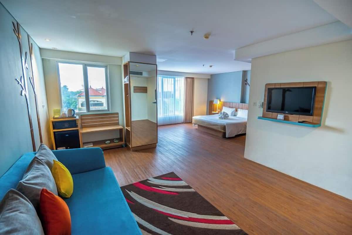 Moderni hotellihuone, jossa on sininen sohva, sänky, televisio ja näkymä ulos.