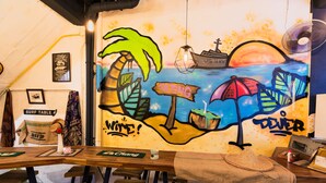A beach-themed mural with palm trees, a sunset, and a surfboard. - Wire Hostel Patong (Patong)