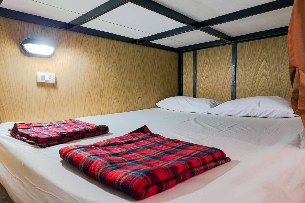 A single bed with two red and blue plaid blankets, a white pillow, and a wooden headboard.