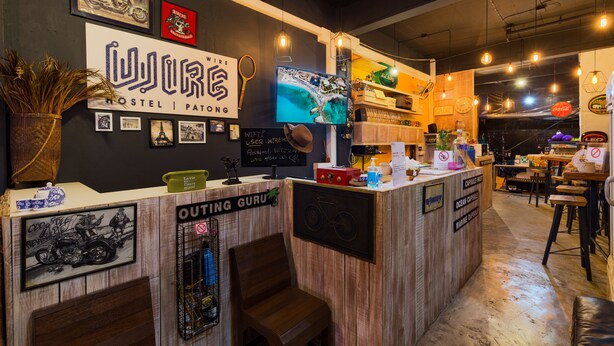 A hostel reception area with a wooden counter, a television, and various framed pictures and signs. - Wire Hostel Patong (Patong)