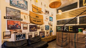 A room with a black leather couch, a wall adorned with motorcycle posters, a wicker hanging light fixture, and a window with a striped blind. - Wire Hostel Patong (Patong)