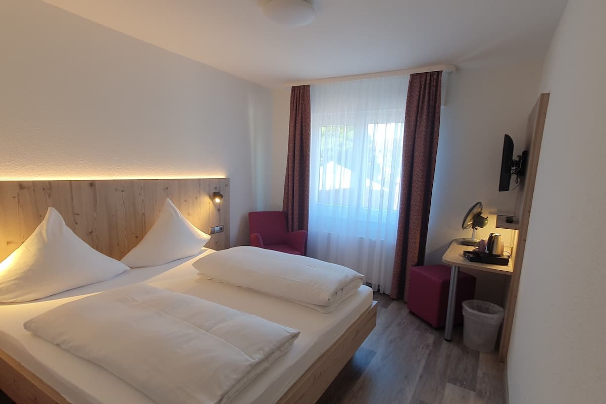 A hotel room with a large bed, a desk with a lamp, and a chair.