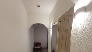 Un couloir étroit au plancher de bois, avec un grand miroir sur le côté droit, et un petit coin salon avec un banc et des coussins au fond.