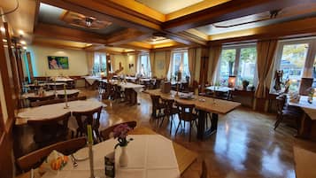 Un comedor amplio con varias mesas y sillas, ventanas grandes y techo de madera.