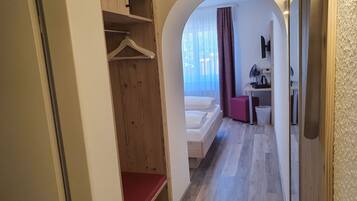 A hotel room with a wooden wardrobe, a bed, a desk with a chair, and a small seating area.