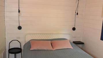 Un dormitorio con cama, una silla, un equipo de aire acondicionado y techo de madera.