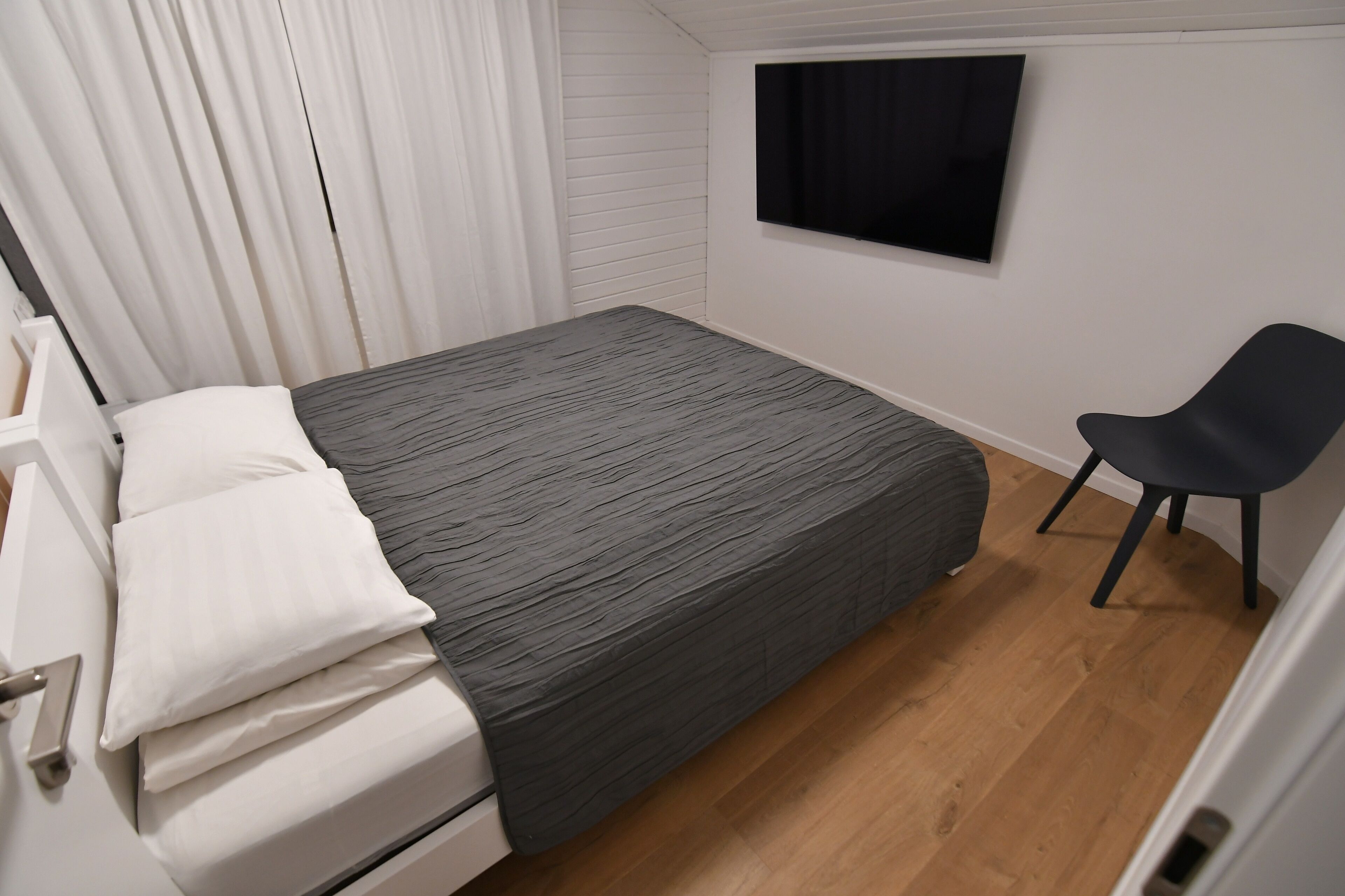 Un dormitorio con cama, una silla, un televisor y una ventana con cortinas.
