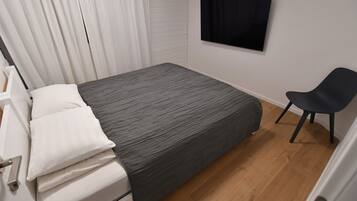 Un dormitorio con cama, una silla, un televisor y una ventana con cortinas.