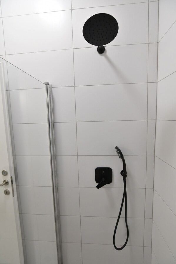 Zona de ducha con cabezal de ducha de mano y otro fijo en una pared de azulejos.