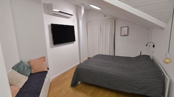 A bedroom with a bed, a TV mounted on the wall, an air conditioning unit, and a window with curtains.