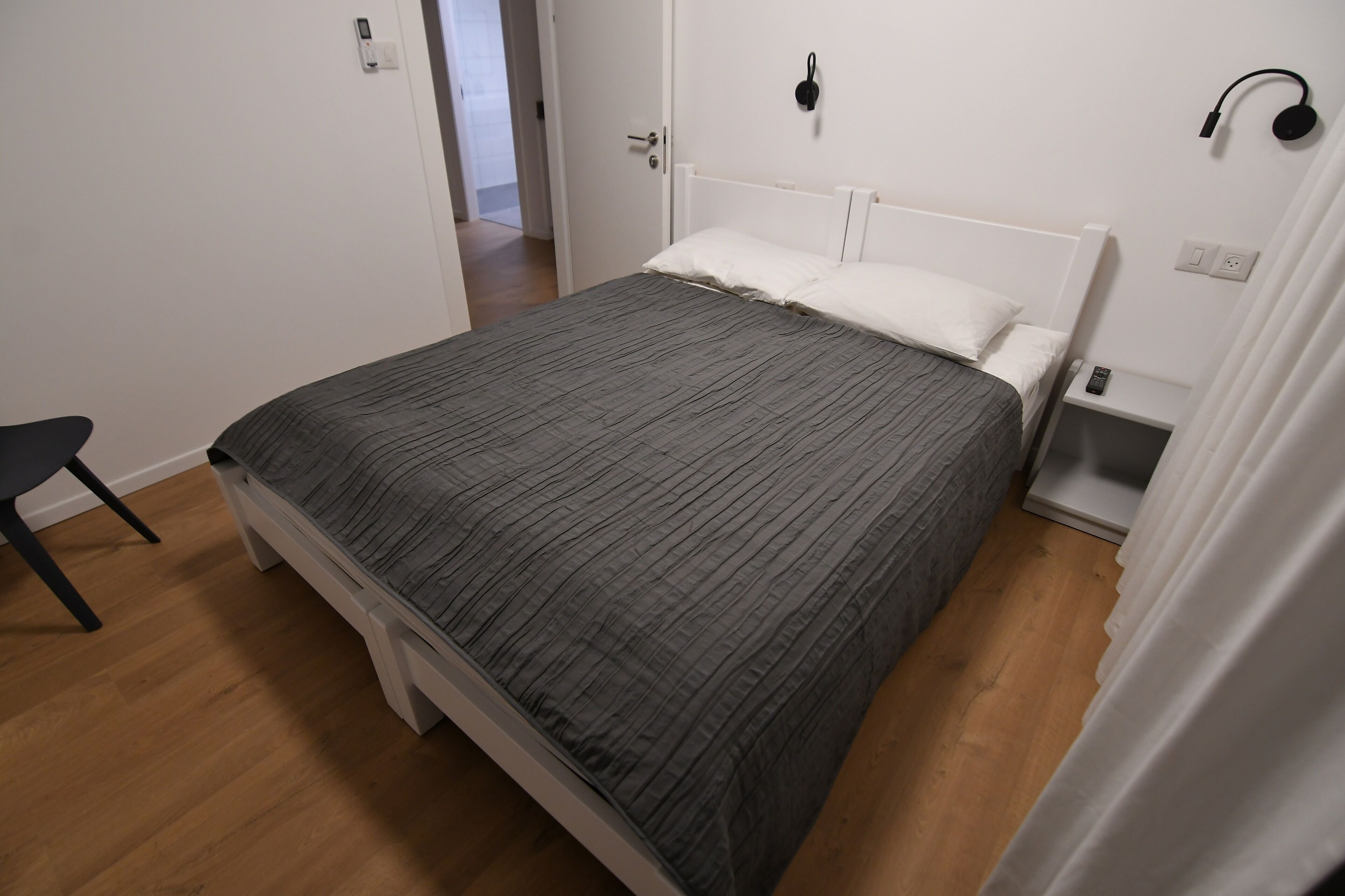 Un dormitorio con cama, una silla, una mesita de noche y una lámpara de pared.