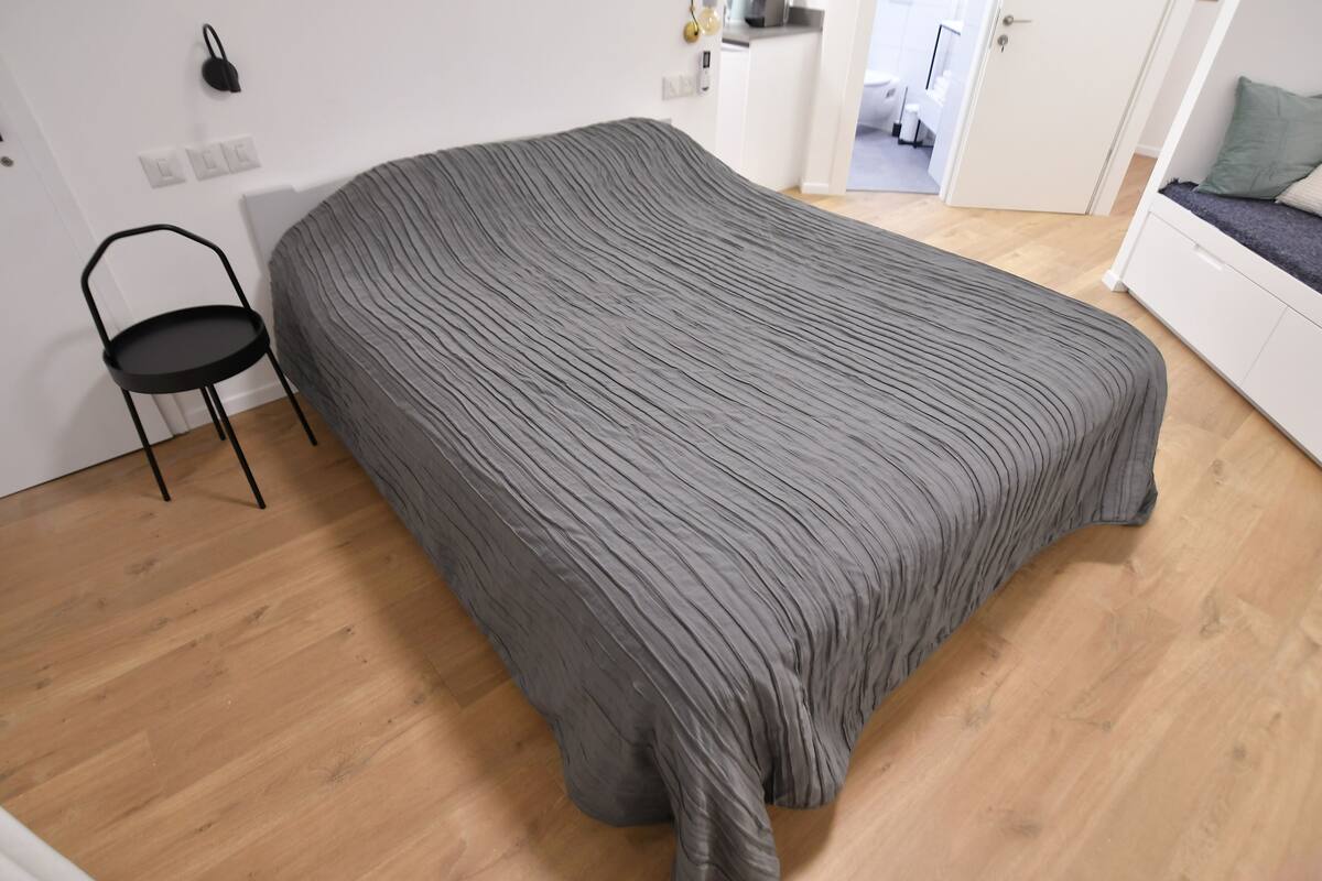 Ein Schlafzimmer mit einem Bett, einem Sessel und einer Küchenzeile im Hintergrund.