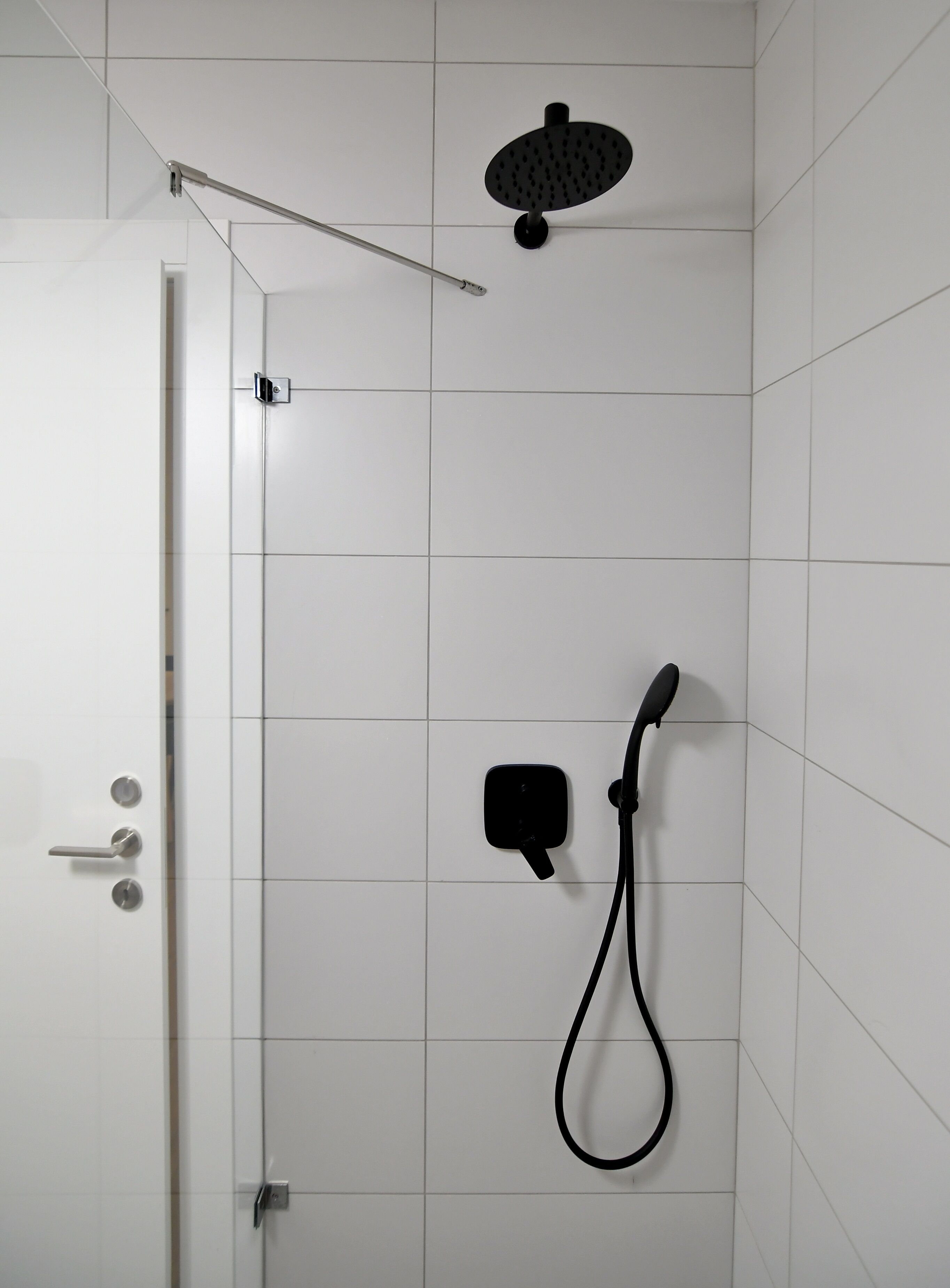 A shower with a handheld showerhead and a wall-mounted control panel in a tiled room.