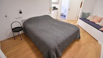 Una habitación con una cama grande, una silla, una kitchenette y un baño visible a través de una puerta abierta.