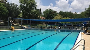 Une piscine d’un bleu éclatant, dotée de séparateurs de couloirs, entourée d’une clôture et ombragée par des auvents bleus.